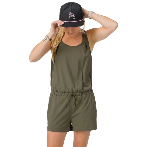 Woman wearing an olive green romper and black cap on a white background